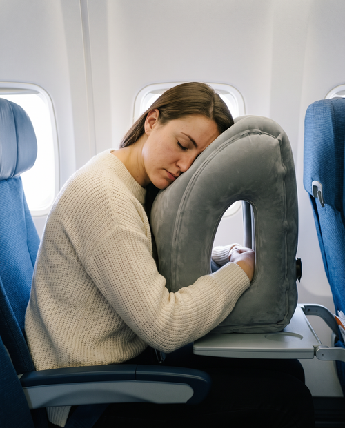 Woman sleeping on a NapHug inflatable travel pillow in an airplane window seat